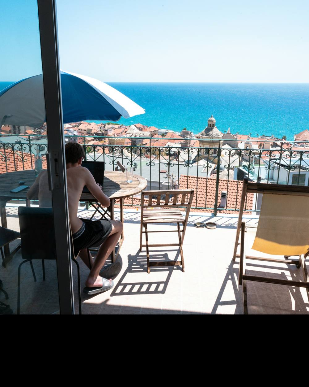 Persona revisando cuentas en el portátil en una terraza con vistas al mar